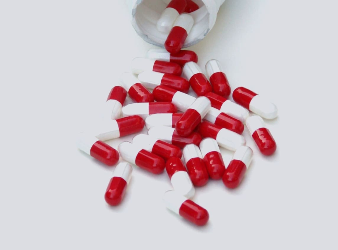 A pile of red and white pills spilled out of a cup.